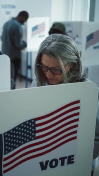 高齢女性の垂直ショットは 投票所のブースで投票に来ます アメリカ合衆国の国民選挙の日 アメリカ合衆国大統領候補の政治的競争 市民の義務に関する概念 スローダウン — ストック動画