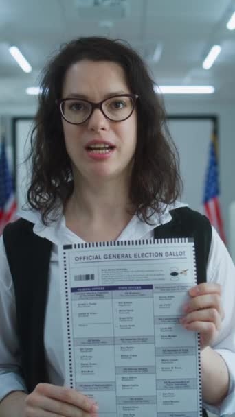 美国妇女的纵向照片在镜头前发言 显示纸片公告 呼吁投票 美国的全国选举日 投票站的投票亭 公民义务的概念和 — 图库视频影像