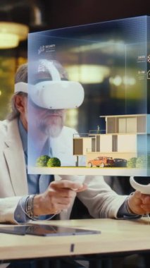 Erkek tasarımcı VR kulaklık ve kablosuz kontrolör kullanır, mimari proje yapar, sanal gerçeklikte ev dış tasarımı yaratır. Modern yüksek teknoloji şirketi. Üç boyutlu hologram. Dikey çekim