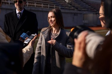 İki organizasyon temsilcisi basın sorularını yanıtlıyor ve dışarıda bir futbol stadyumunda röportaj veriyor. TV haberleri için basın toplantısında başarılı bir SEO röportajı. Gazeteciler basın kampanyasında kalabalıklar.
