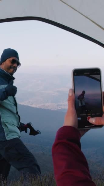 一个女人用电话在美丽的山景上拍了一张游客的照片 手持斧头的非洲裔美国徒步旅行者站在山上 背包客朋友们在探险期间停下来休息 — 图库视频影像