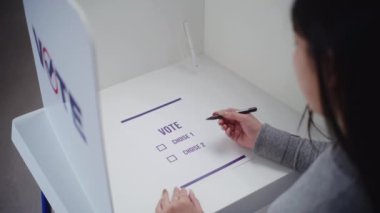 Asyalı kadın sandık merkezindeki oy kabininde duruyor, başkan adayı veya siyasi parti için seçim yapıyor ve oy veriyor. Kadın seçmenler seçimler sırasında gazete bülteni dolduruyor. Vatandaşlık görevi kavramı.