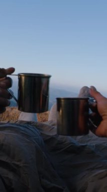 Romantik turist çiftler dağ tepesinde çadırda uzanır, bardaklarını tokuşturur ve çay içerler. İki gezgin macera tatili sırasında battaniye altında dinleniyor. Yürüyüş ailesi soğuk havada ısınır ve manzaraya hayran kalır..