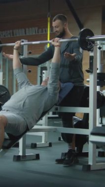 Modern spor salonunda halterli protez bacak egzersizleri ve kişisel fitness koçu olan dikey nişancı. Yapay bacaklı bir atlet spor ekipmanları kullanarak ağırlık çalışması yapıyor. Fiziksel