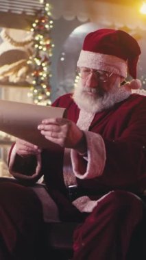 Sakallı Noel Baba 'nın parşömende kitap okuyup gülerken elflerin aydınlık atölyede Noel kutlaması için hediyeler hazırlayışına odaklan. Dikey çekim