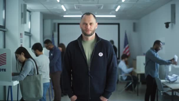 Człowiek Odznaką Stoi Nowoczesnej Lokalu Wyborczym Pozuje Uśmiecha Się Patrzy — Wideo stockowe