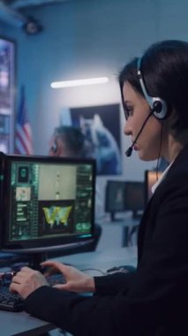 Uçuş kontrol merkezinde roket fırlatma üzerinde çalışırken bilgisayar klavyesine kulaklık takan genç bir kadın. Dikey çekim