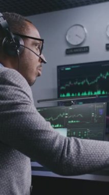 Elinde kalem olan Afrikalı Amerikalı yatırımcı bilgisayarda gerçek zamanlı hisse senedi sergiliyor. Meslektaşlar, arka plandaki büyük ekranlardaki döviz piyasalarının grafiklerini analiz ederler. Ticaret ve yatırım kavramı.