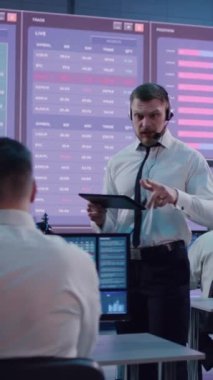 Kulaklığı ve tableti olan, kravatını düzelten ve borsa ofisindeki borsa simsarlarına talimat veren sakallı sinirli bir adamın dikey çekimi.