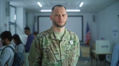 Erkek askerin portresi, Amerika Birleşik Devletleri seçmeni. Kamuflaj üniformalı bir adam modern bir seçim merkezinde duruyor ve kameraya bakıyor. Oy verme kabinleri olan bir arka plan. Vatandaşlık görevi kavramı.