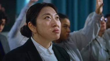 Asyalı kadın gazetecinin portresi soru sormak için elini kaldırıyor, basın kampanyası sırasında politikacının konuşmasını dinliyor. Çeşitli medya temsilcileri röportaj sırasında parlamento konferans salonunda oturuyorlar