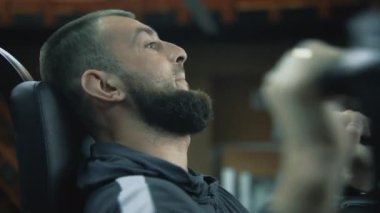 Sporcu, modern spor ya da fitness merkezindeki makinede derin bir şekilde nefes alır. Formda adam, profesyonel spor ekipmanları kullanarak silah için güç egzersizleri yapıyor. Spor ve fiziksel aktivite. Portre.