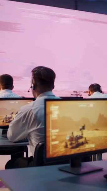 年轻的女员工坐在控制室同事旁边的办公桌前 头戴耳机 在电脑键盘上打字 看火星研究车的视频 垂直射击 — 图库视频影像