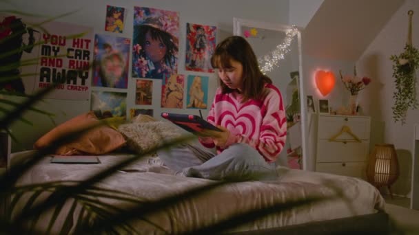 在舒适的卧室里 亚洲少女坐在床上 用平板电脑和数字铅笔在网上画画或冲浪 女孩在家里消磨时光 玩得很开心 生活方式概念 — 图库视频影像