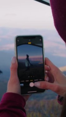 Kadın, telefon kullanarak güzel bir dağ manzarasında turistin fotoğrafını çekiyor. Elinde balta olan Afrikalı Amerikalı yürüyüşçü tepede poz veriyor. Gezginler macera tatili sırasında dinlenmek için durdular. Dikey çekim