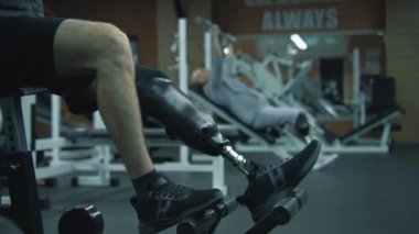 Modern spor salonunda protez bacak egzersizleri yapan motive bir sporcu. Fiziksel engelli atletik beyaz adam profesyonel spor ekipmanları kullanarak silah eğitimi yapıyor..