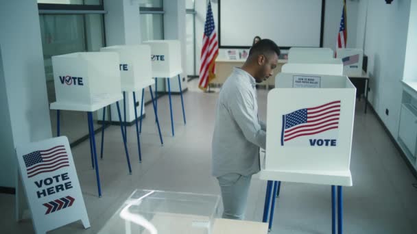アフリカ系アメリカ人男性が投票所で投票ブースで大統領候補に投票し 投票用紙を箱に入れる アメリカ合衆国の国民選挙の日に男性米国市民 市民としての義務 — ストック動画
