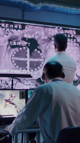 ミッションコントロールセンターの大画面で軌道上の駅にドッキング宇宙船を見て匿名の演算子のチームのパンの右側のビュー — ストック動画