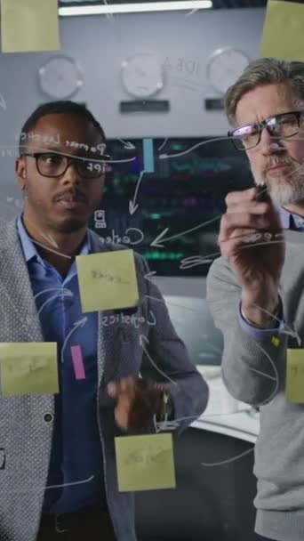 多人種金融アナリストは 投資銀行のオフィスでガラス壁に描画し 会社の暗号ビジネス戦略を開発して分析します コンピュータと背景にリアルタイム株式を持つ大きなデジタル画面 — ストック動画