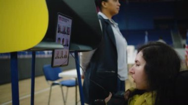 SMA engelli bir kadın oy kullanmak için uzaktan kumanda ve tablet bilgisayar kullanıyor, sandık merkezinde oy kullanıyor. Tablet ekranda gösterilen ABD başkan adaylarının listesi. ABD 'de seçimler.