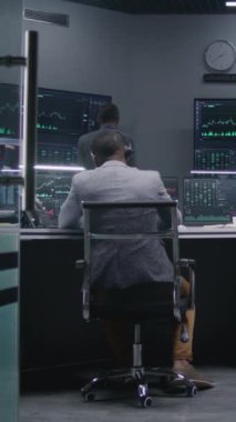 Çok ırklı finansal analistlerden oluşan bir ekip, modern ofiste gerçek zamanlı sergilenen hisselerle bilgisayar üzerinde çalışıyor. Meslektaşlar büyük ekranlarda döviz piyasalarının grafiklerini analiz ederler. Yatırım ve ticaret. Dikey