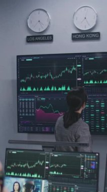 Mali analistlerden oluşan ekip, birçok büyük ekranda döviz piyasası grafiklerini analiz ediyor. Gerçek zamanlı sergilenen hisse senetleriyle bilgisayar başında çalışan Afro-Amerikan bir adamı vurdu. Dikey çekim