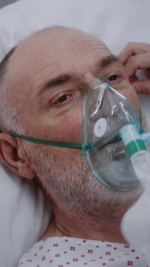Hemşire hasta kıdemli hastayla ilgileniyor. Oksijen maskeli yaşlı adam yapay akciğer havalandırması sırasında yatakta yatıyor. Modern hastanenin acil servisi. Klinikte yoğun bakım Coronavirus Bölümü.