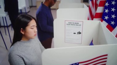 Oy pusulası olan Asyalı kadın seçmen sandık merkezindeki oy kullanma kabinine gelir, seçim yapar ve başkan adayı için oy verir. ABD 'de Ulusal Seçim Günü' nde ABD vatandaşı.