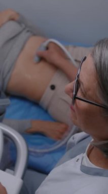 Dikey iğne uzmanı, doktor karın organlarını dijital monitörlü ultrason cihazı kullanarak kadın hastaya kontrol ediyor. Yetişkin kadın modern klinikte sonografi kontrolünden geçiyor..