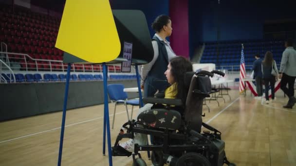 身体障害を持つ米国の女性投票者は 投票のためにリモートコントロールとタブレットコンピュータを使用しています ポーリングステーションで車椅子の投票でSmaを持つ女性 アメリカ合衆国大統領選挙 — ストック動画