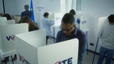 AB seçimleri sırasında sandık merkezinde oy kullanan çok ırklı Avrupalı insanların yüksek açısı. Çeşitli seçmenler oy kullanma kabinlerinde oy kullanırlar. Avrupa Birliği 'nde Seçim Günü. Vatandaşlık görevi ve demokrasi.