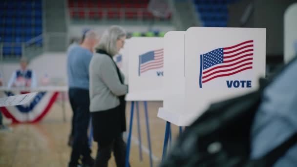 手元に掲示された高齢男性の有権者は投票ブースに来ます 多文化系アメリカ人が投票所で投票する アメリカ合衆国大統領候補の政治的競争 — ストック動画