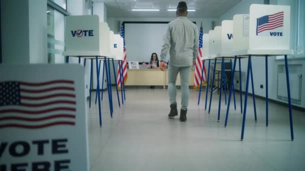 米国市民 アフリカ系アメリカ人男性有権者は 投票所に登録するために女性の投票官に歩き 投票のための論文掲示書を取ります アメリカ合衆国選挙の日 — ストック動画
