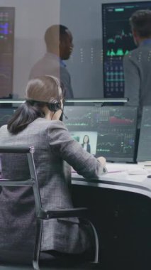 Çeşitli finansal analistler bilgisayarlardaki gerçek zamanlı hisse senetlerini izliyor. İş adamlarından oluşan bir ekip banka ofisinde çalışıyor. Döviz piyasası grafiklerini gösteren büyük dijital ekranlar. Dikey çekim