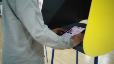 ABD vatandaşı oy vermek için tablet bilgisayar kullanıyor. Afrika kökenli Amerikalı, erkek seçmen seçim yapıyor ve oy verme kabininde oy kullanıyor. Amerika Birleşik Devletleri Başkanlık Seçimi. Yurttaşlık görevi.