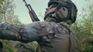 Siperlerde taktik teçhizat kullanan erkek asker ya da savaşçı ormanda saldırıya ya da çatışmaya hazır otomatik tüfek için dolu şarjörler alır. Silahlı kuvvetler. Savaş ya da askeri çatışma konsepti.