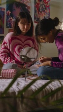Afrikalı Amerikalı kız sevimli Asyalı arkadaş yüzüne makyaj yapıyor. İki çok kültürlü genç kız yatak odasında oturup birlikte eğleniyorlar. Şık bir iç dekorasyonu olan rahat bir ev. Dikey çekim
