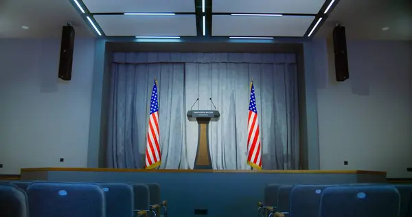 stock image Tribune for President of the United States political speech in the White House. Press campaign room with seats. Wooden conference debate stand with microphones on stage. American flags in background.