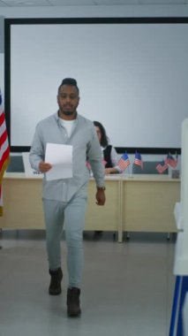 Afro-Amerikalı adamın dikey çekimi oy kullanma merkezindeki kadın oy pusulasından oy pusulasına gidiyor ve oy kabinine gidiyor. Amerika Birleşik Devletleri 'nde Ulusal Seçim Günü. Vatandaşlık görevi