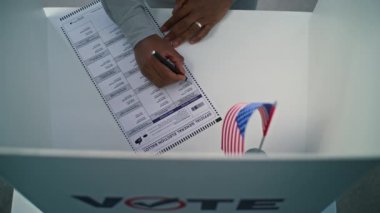 ZAPORIZHYA, UKRAINE - 15 Mart 2024: Amerikan bayrağıyla oy verme kabininde oy pusulasını dolduran anonim ABD vatandaşının kapanışı. Afro-Amerikalı adam anketlerde başkan adaylarına oy verdi