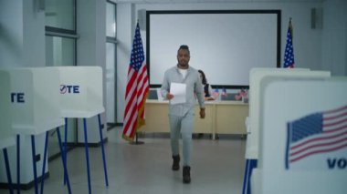 Afro-Amerikalı adam oy kullanma merkezindeki oy kullanma memurundan oy almak için kağıt oy kullanıyor. Amerikan vatandaşı bülteni doldurmak için oy kabinine yürüyor. Amerika Birleşik Devletleri 'nde seçim günü. Yurttaşlık görevi.