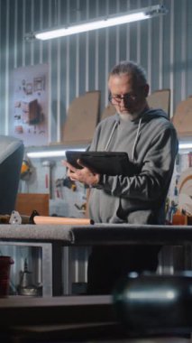 Olgun marangoz veya tasarımcı dijital tablet kullanır ve modern atölyede sandalye ile mobilya yapmak ve yenilemek için çalışır. Bir başka uzman raf montajı yapıyor. El yapımı ve girişimcilik kavramı.