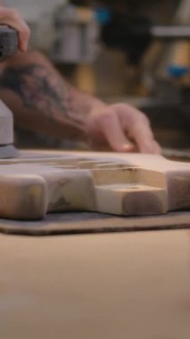 Erkek marangozun, iş yerindeki tahta gitar vücudunu parlatırken yakın plan fotoğrafı. Ahşap ustası, zanaatkar modern atölyede müzik aleti yapıyor. Dikey çekim