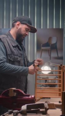 Profesyonel marangoz, profesyonel aletlerle LED lambanın altında ahşap komodin monte eder. Erkek zanaatkar, esnaf mobilya yapmak için modern atölyede çalışıyor. El işi ve küçük işletme konsepti.