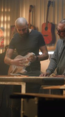 İki profesyonel marangoz ahşap gitar yapar ve ölçü alır. Modern atölyede müzik aletleri yapan sanatçılar. İş arkadaşı arka planda çalışıyor. El yapımı ve girişimcilik..