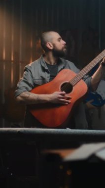 Erkek zanaatkar akustik gitar çalar, sesi kontrol eder. Ahşap ustası, marangoz modern atölyede ahşap müzik aleti yapıyor. Meslektaşlar arka planda çalışır. Dikey çekim