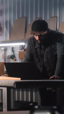 Erkek marangoz, tasarımcı dijital tablet ve dizüstü bilgisayar kullanıyor, modern atölyede mobilya yapımı ve yenilenmesi için sandalyeyle çalışıyor. Olgun uzman arka planda rafları birleştirir. El yapımı konsept.