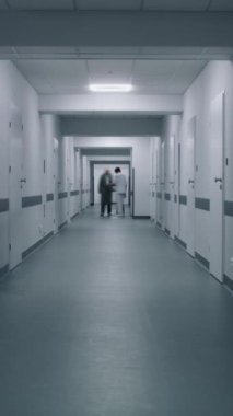 Tıp merkezi koridorunda yürüyen hekim ve hastaların zaman aşımı. İnsanlar hastane koridorundaki doktorlarla görüşmeye geliyor. Klinikte çok ırklı sağlık uzmanları çalışıyor. Dikey çekim.