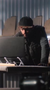 Erkek marangoz, tasarımcı, mobilya yapmak için şık bir atölyede tablet bilgisayar ve dizüstü bilgisayar kullanarak şairin tasarımını yapıyor. İş arkadaşı arka planda çalışıyor. El işi ve küçük işletme konsepti.