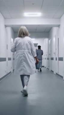 Hasta tedavi geçmişi olan beyaz üniformalı doktor hastane koridorunda yürüyor. Arka planda çok ırklı sağlık uzmanları var. Tıbbi personel klinikte çalışıyor. Dolly vurdu. Dikey